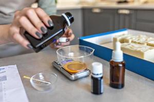 A soap-maker woman weighs aromatic oils for making cosmetics on a kitchen scale. Home spa. Small business photo