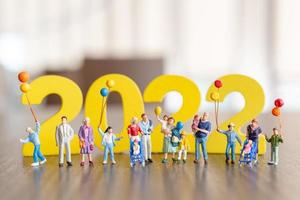 Gente en miniatura familia feliz sosteniendo globo en blanco número 2022 foto