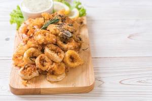 Fried seafood of squid, shrimp, mussels with sauce on wooden board photo