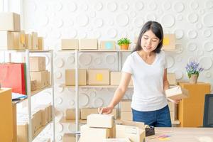 Mujer asiática propietaria de una empresa que trabaja en casa con una caja de embalaje en el lugar de trabajo - emprendedor pyme de compras en línea o concepto de trabajo independiente