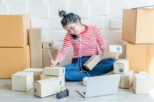 Mujer asiática propietaria de una empresa que trabaja en casa con una caja de embalaje en el lugar de trabajo - emprendedor pyme de compras en línea o concepto de trabajo independiente
