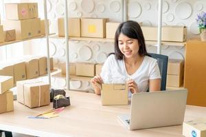 Asian woman business owner working at home with packing box on the workplace - online shopping SME entrepreneur or freelance working concept photo