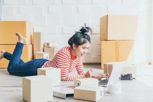 Asian woman business owner working at home with packing box on the workplace - online shopping SME entrepreneur or freelance working concept