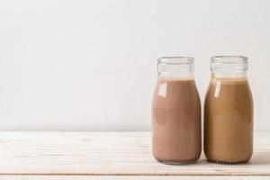 Chocolate milk and coffee with milk in bottle on wood background photo