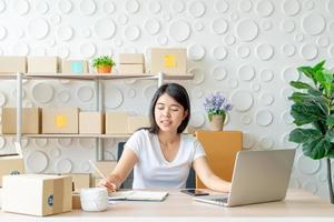 Joven mujer asiática puesta en marcha de una pequeña empresa que trabaja con una tableta digital en el lugar de trabajo: venta en línea, comercio electrónico, concepto de envío