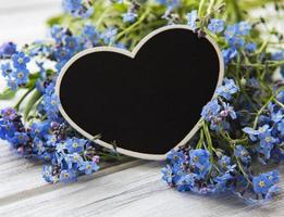 Forget-me-not flowers and black heart shaped board on white wooden background photo