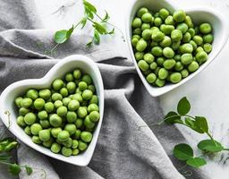 Green peas in heart shaped bowls on a fabric background photo