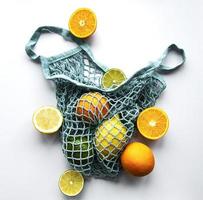 Ripe whole citrus fruits in string bag on white background photo