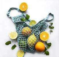 Ripe whole citrus fruits in string bag on white background photo