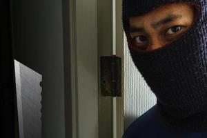 Masked robber with knife hiding behind the door photo
