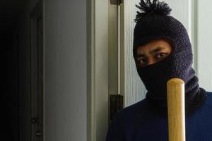 Masked robber with baseball bat hiding behind the door photo