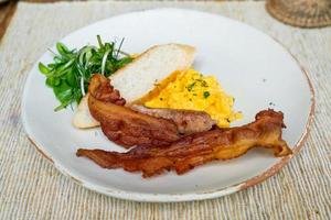 revuelve egga con tocino y salchichas en un plato para el desayuno foto