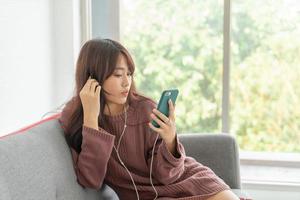 Beautiful Asian woman using smartphone on grey sofa in living room