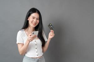 Mujer asiática joven que usa el teléfono con la mano que sostiene la tarjeta de crédito - concepto de compras en línea foto
