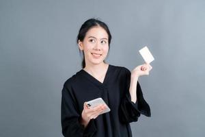 Young Asian girl showing plastic credit card while holding mobile phone photo