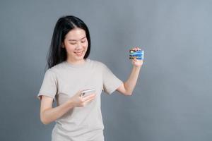 Young Asian girl showing plastic credit card while holding mobile phone photo