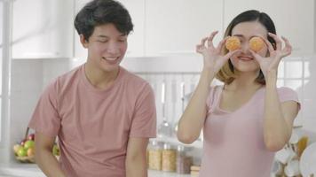 heureux asiatique belle jeune famille couple mari et femme appréciant le sourire et le rire tient une orange coupée devant les yeux du gars qui passe du temps ensemble dans la cuisine à la maison. ralenti