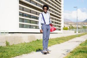 Black businessman riding skateboard near office building. photo