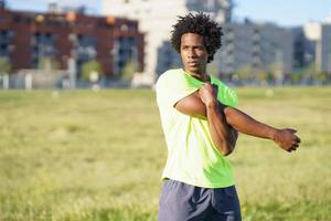 Hombre negro con cabello afro haciendo estiramientos después de correr al aire libre. foto