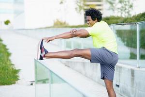 Hombre negro con cabello afro haciendo estiramientos después de correr al aire libre. foto