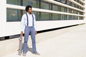 macho negro de pie junto a un edificio de oficinas con una patineta. foto