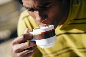 Hombre negro disfrutando de un café en la cafetería mientras está sentado en la mesa al aire libre foto
