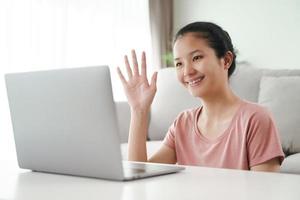 mujer joven con ordenador portátil para videoconferencia agitando el gesto de la mano. foto