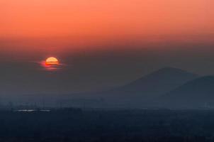 Atardecer con siluetas de colinas en el fondo, sol cubierto por nubes foto