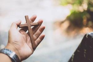 mano que sostiene la cruz de madera con fondo borroso foto