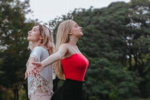 Two women standing and rise up hands at park. Best friends photo