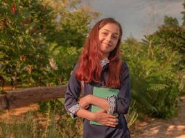 colegiala en un vestido de la escuela con un cuaderno y una mochila al aire libre foto