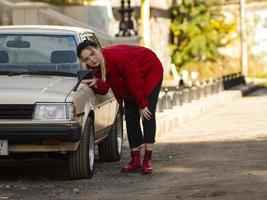 Joven rubia vestida de rojo está mirando en el espejo de un coche viejo foto