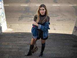 slender blonde girl stands on the stairs on the street photo