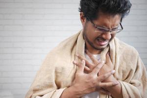 Mature man in blanket coughing while sited on bed photo