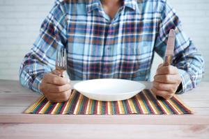 Mano sujetando cubiertos con plato vacío en la mesa de madera foto