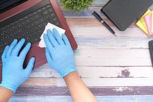 hand in blue rubber gloves and white tissue disinfecting keyboard photo