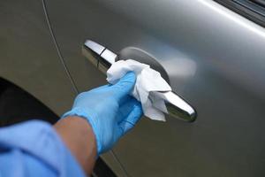 Mano en guantes azules limpiando la perilla de la puerta del coche con un pañuelo foto