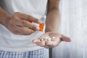 La mano del hombre con la medicina derramada fuera del contenedor de pastillas foto