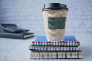 take away paper cup on stack of notepad on table photo