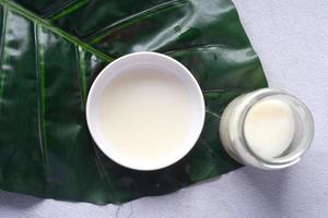 coconut oil in a container and a leaf on table photo
