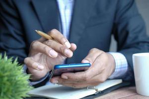 young man hand using smart phone and writing on notepad at desk photo