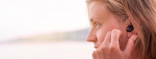 Mujer con auriculares inalámbricos, junto al mar en el fondo foto