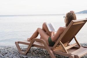 The beautiful young woman lying on the sun lounger reading a book photo
