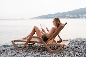 The beautiful young woman sitting on the sun lounger reading a book photo