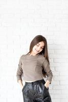 woman on white brick wall background holding hands in pockets photo