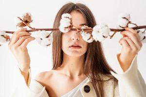 Beautiful woman in cozy clothes holding branch of cotton flowers photo