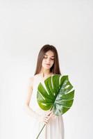 Happy beautiful woman in cozy clothes holding a green monstera leaf photo