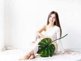 Feliz hermosa mujer en ropa acogedora sosteniendo una hoja de monstera verde foto