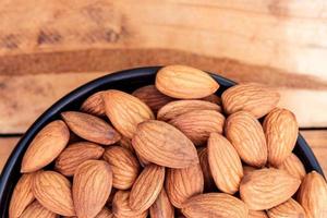 Close up raw peeled almonds seed in bowl on wooden background photo