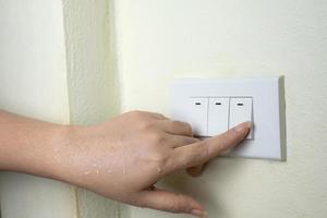Mano mojada encienda las luces interruptor eléctrico sobre fondo de pared blanca foto